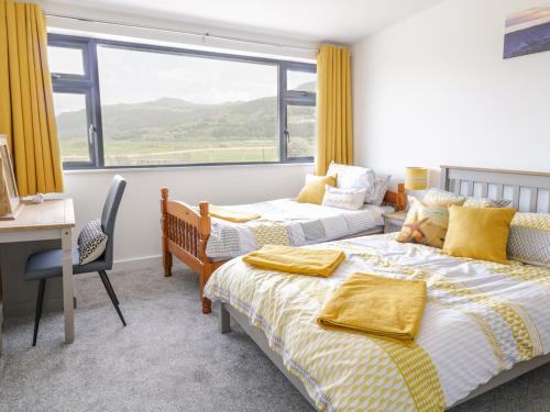 two beds in a room with a desk and a window at Llarios in Fairbourne