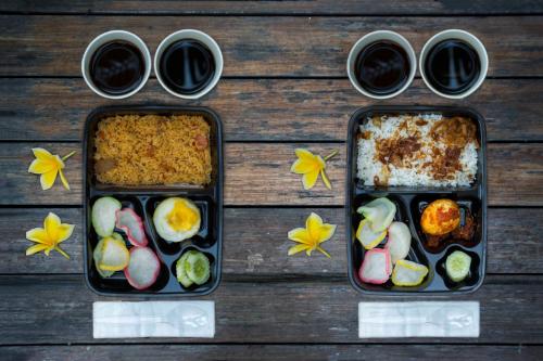 three bento boxes filled with food on a wooden table at Titanium Express HomTel in Jakarta