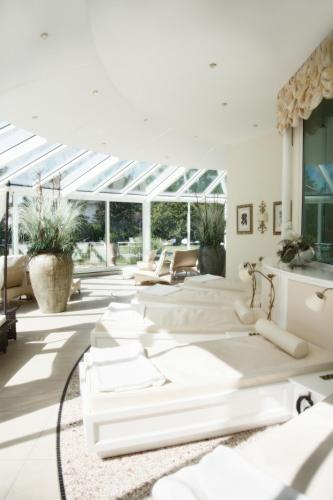 a living room with white furniture and large windows at Thermenhotel Quellenhof in Bad Füssing
