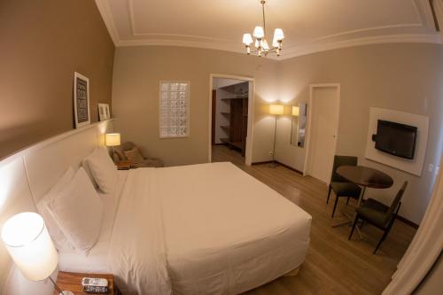 a bedroom with a large white bed and a table at Planalto Select Hotel Ponta Grossa in Ponta Grossa