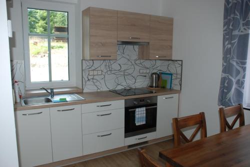 eine Küche mit weißen Schränken, einer Spüle und einem Tisch in der Unterkunft Apartmán Raketa in Pernink