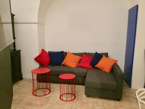 un sofá con almohadas coloridas y 2 mesas rojas en Ostuni dans le vieux bourg, maison sur la Piazzetta, en Ostuni