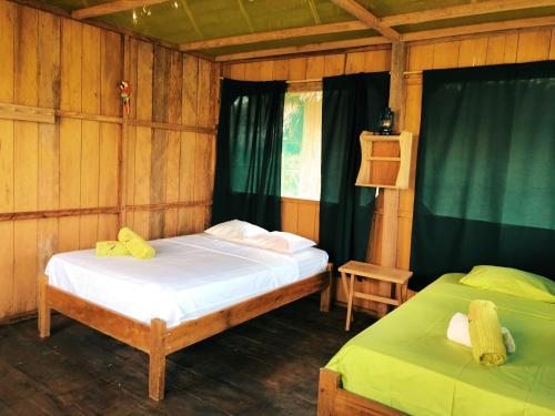 Cette chambre en bois comprend 2 lits et des rideaux verts. dans l'établissement Iguana Lodge Perú, à Iquitos