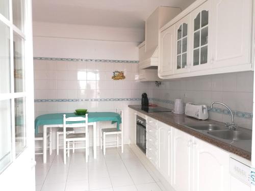 a kitchen with white cabinets and a table and chairs at Vivenda Framboesa in Vila Nova de Milfontes