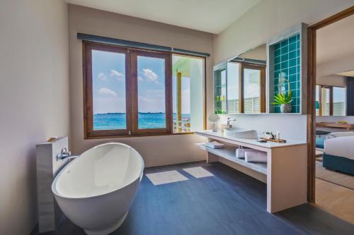 a bathroom with a tub and a bed and a sink at Dhigali Maldives - A Premium All-Inclusive Resort in Raa Atoll