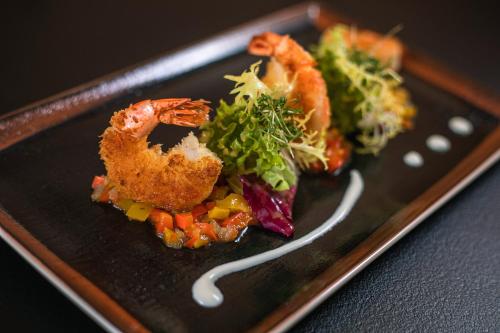 a black plate of food with shrimp and vegetables at Hotel Amberger Hof in Bad Koetzting