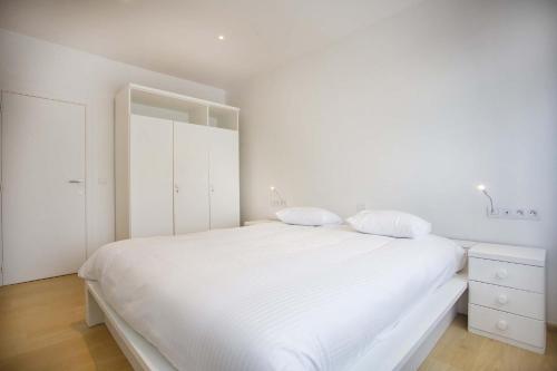 a white bedroom with a large white bed with two pillows at Huize Mamoesh in De Panne