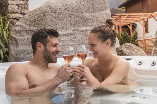a man and woman drinking champagne in a bathtub at Feldmilla Design Hotel - Wellness & SPA in Campo Tures