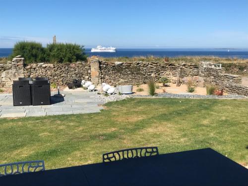 a yard with a stone wall and a ship in the distance at Le Clos de la Pointe Saint-Mathieu in Plougonvelin