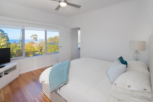 a white bedroom with a bed and a flat screen tv at Casa Azzura - beachside entertainer in Dunsborough
