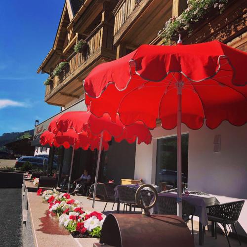 a group of tables with red umbrellas in front of a building at Romantik Villa Cesanueva in Selva di Val Gardena