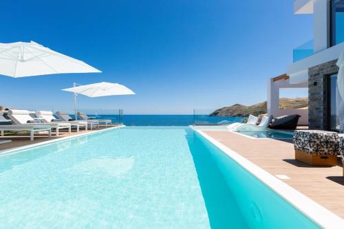 Una piscina con sillas y sombrillas y el océano. en Wave Villa, Seaside Living & Your Own Beach Spot, By ThinkVilla, en Panormos Rethymno
