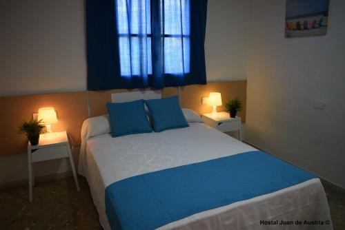 a bedroom with a bed with blue pillows and a window at Hostales Juan de Austria I & II in Aguadulce