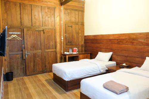 two beds in a room with wood paneling at Pendhapa Art Space - PAS Limasan Homestay in Yogyakarta