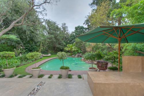 a pool with a green umbrella and a chair and a table at The Lemon Tree Self- Catering in Johannesburg