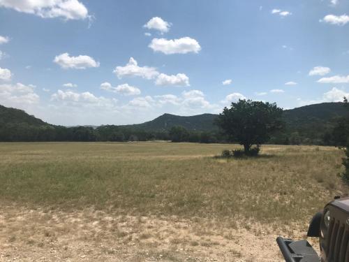 a field with a tree and mountains in the background at A Peace of Heaven Cabins and RV in Vanderpool