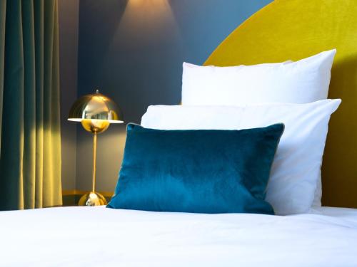 a bed with white pillows and a blue pillow at Hotel Mercure Roscoff Bord De Mer in Roscoff