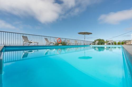 a large swimming pool with an umbrella and two chairs and an umbrella at Villa Panoramica II in Arco da Calheta