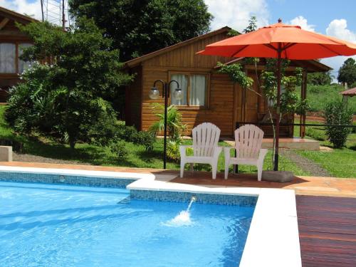 two chairs and an umbrella next to a pool at Cabañas Doralia in Oberá