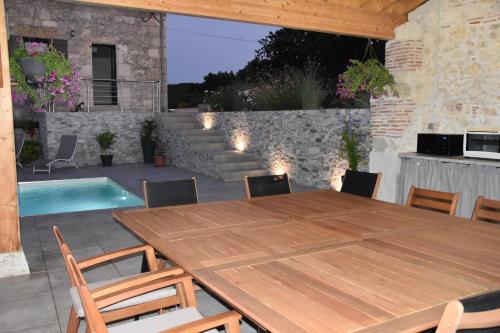 a wooden table and chairs on a patio with a pool at Domaine de calbiac in Dolmayrac