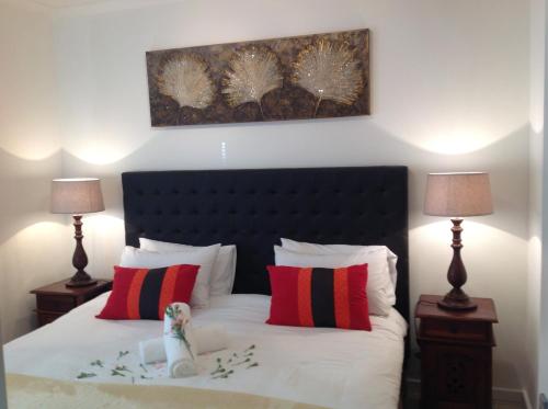 a bedroom with a bed with red and black pillows at Secret Garden Guesthouse in Bloubergstrand
