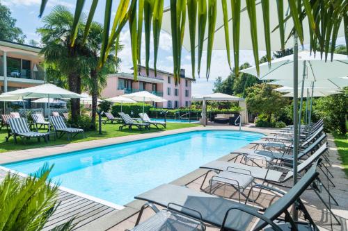 uma piscina com espreguiçadeiras e guarda-sóis em Hotel & Spa Cacciatori em Cademario