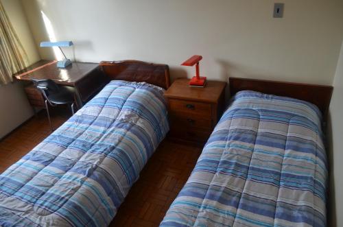 two beds in a bedroom with a desk and a lamp at Pousada das Orquideas de Jau in Jaú