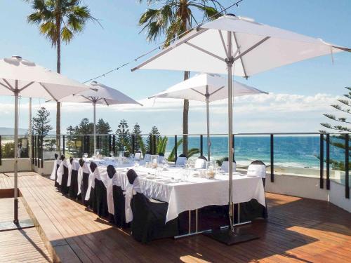 a dining table with white umbrellas and the ocean at Novotel Wollongong Northbeach in Wollongong
