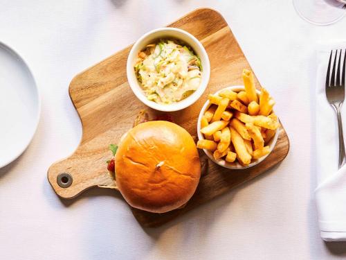 a wooden cutting board with a sandwich and french fries at Mercure Newbury West Grange Hotel in Thatcham