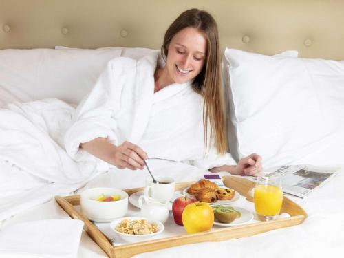a woman laying in bed with a tray of food at Mercure Luxembourg Kikuoka Golf & Spa in Canach