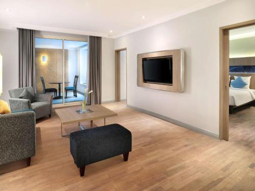 a living room with a couch and a tv on a wall at Novotel Jakarta Mangga Dua Square in Jakarta