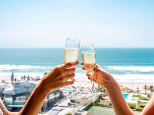 two people holding champagne glasses in front of the beach at Novotel Surfers Paradise in Gold Coast
