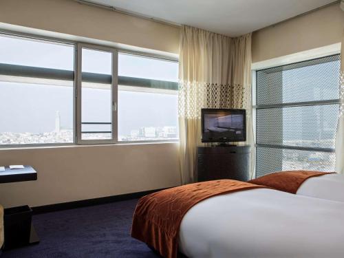 a hotel room with a bed and a tv and windows at Sofitel Casablanca Tour Blanche in Casablanca