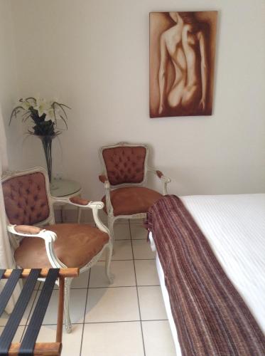 a bedroom with two chairs and a bed and a painting at Welcome Guest House in Vereeniging