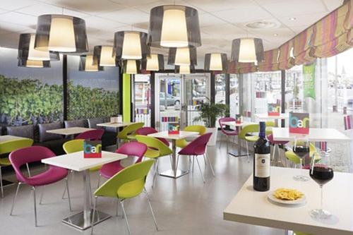 um restaurante com cadeiras e mesas coloridas e uma garrafa de vinho em ibis Styles Bordeaux Saint Médard em Saint-Médard-en-Jalles