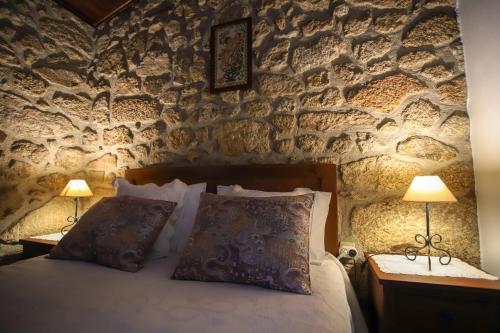 a bedroom with a stone wall with a bed and two lamps at Casas da Lagariça in Sortelha