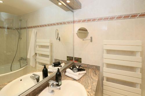 ein Badezimmer mit einem Waschbecken, einer Badewanne und einem Spiegel in der Unterkunft Aparthotel Adagio Geneve Saint Genis Pouilly in Thoiry