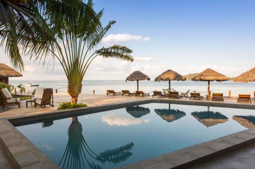 a pool with chairs and umbrellas next to the ocean at Corail Noir Hotel in Ambaro