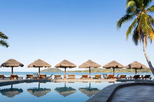 a pool with chairs and umbrellas on the beach at Corail Noir Hotel in Ambaro