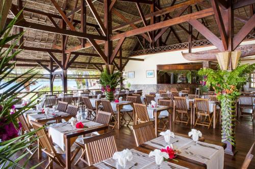 a restaurant with wooden tables and chairs and plants at Corail Noir Hotel in Ambaro