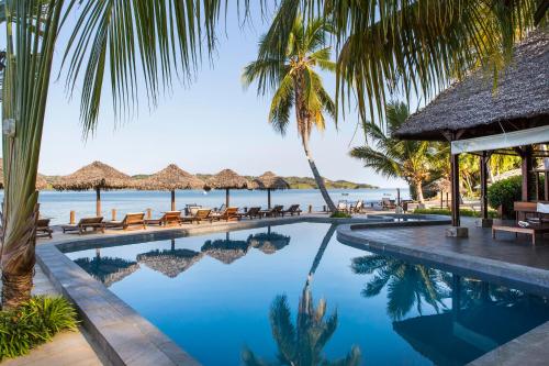 a pool at a resort with palm trees and the ocean at Corail Noir Hotel in Ambaro