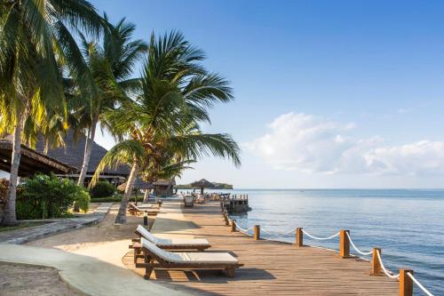 a beach with chairs and palm trees and the ocean at Corail Noir Hotel in Ambaro
