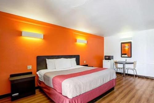 1 dormitorio con pared de color naranja, cama y mesa en Scottish Inns & Suites, en Texas City