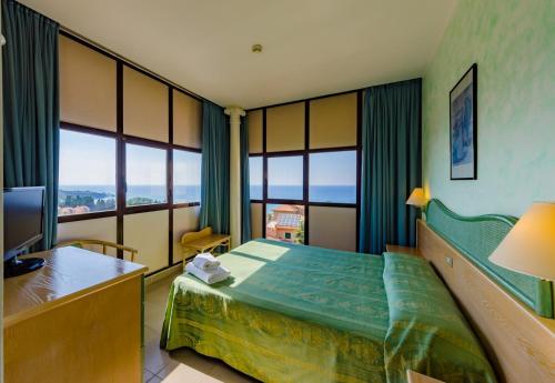 sypialnia z łóżkiem, telewizorem i oknami w obiekcie Hotel Villa Belvedere w Cefalù