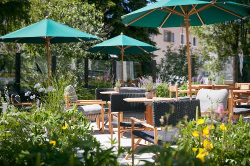 un patio con mesas, sillas y sombrillas en Hotel Walther - Relais & Châteaux en Pontresina
