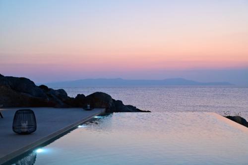 a swimming pool next to the ocean at sunset at Kavos Hotel & Suites in Stavros