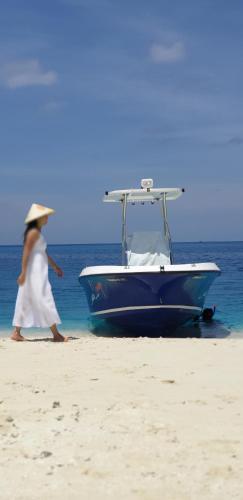 a woman walking on the beach next to a boat at Luau Beach Inn, Maldives in Fulidhoo