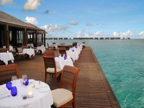 a restaurant on the water with white tables and chairs at The Residence Maldives in Gaafu Alifu Atoll