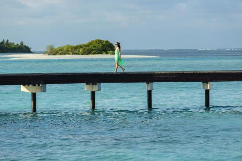 a woman walking on a dock in the water at The Residence Maldives in Gaafu Alifu Atoll