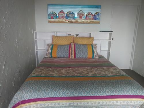 a bed in a bedroom with a painting on the wall at La Casa Te Puru Lodge in Te Puru